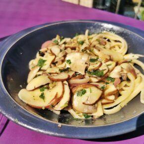 Linguine mit Champignons und Petersilie auf einem blaugrauen Teller auf einem violetten Tisch in der Sonne.