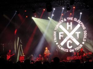 Frank Turner and the Sleeping Souls auf der Bühne vor dem Bendschriftzug und dem FTHC-Cross (Frank Turner Hardcore)
