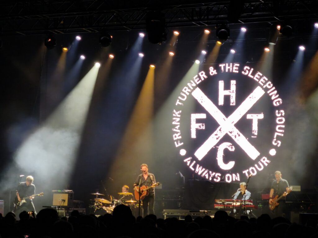 Frank Turner and the Sleeping Souls auf der Bühne vor dem Bendschriftzug und dem FTHC-Cross (Frank Turner Hardcore)