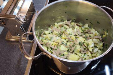 Kochfeld mit einem Edelstahltopf, der mit Krautfleckerl mit Buchweizennudeln und reichlich Petersilie gefüllt ist, daneben eine Nudelmaschine